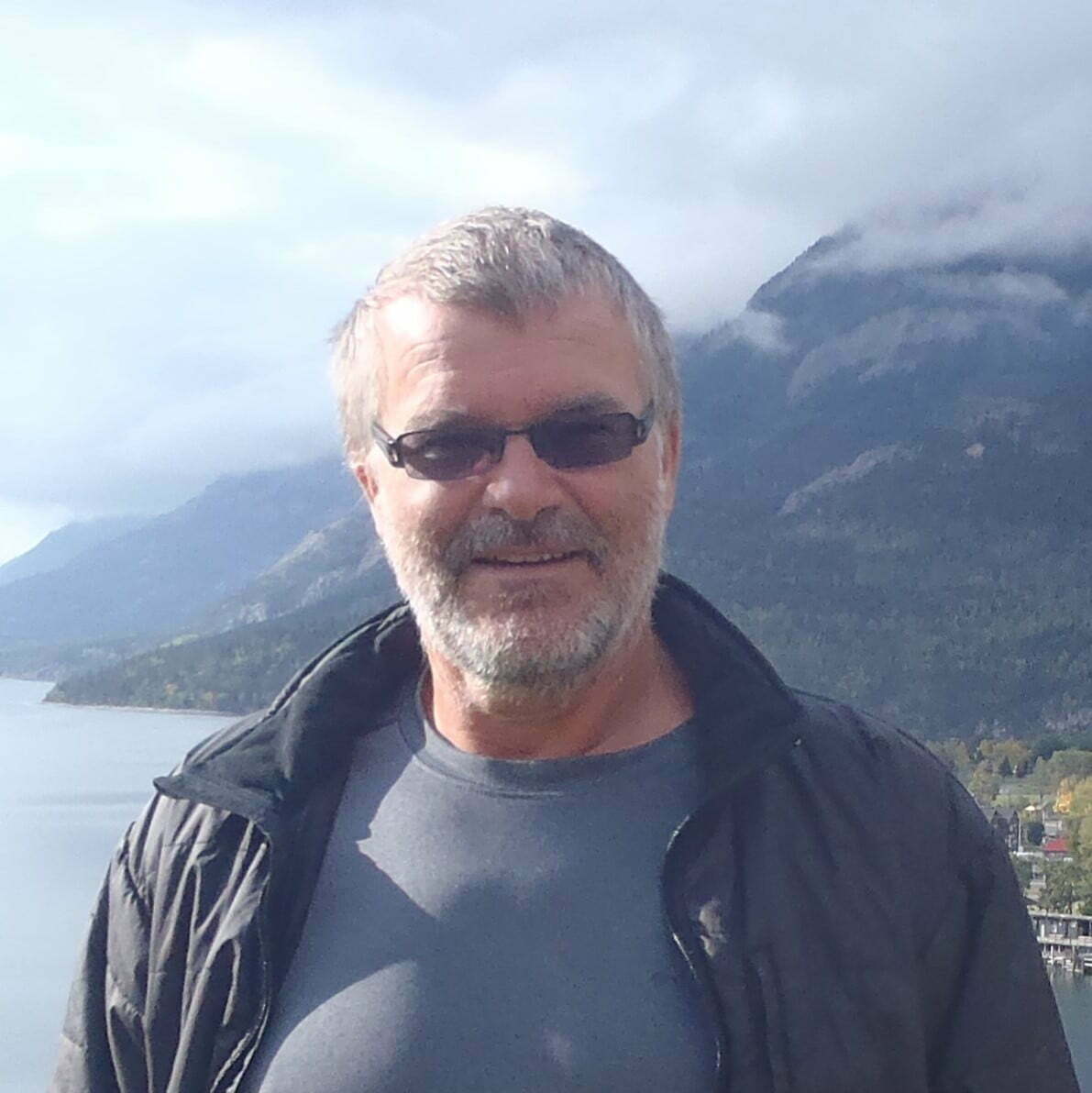 Neil Van der Putten photo to man in front of sea side town in distance with mountains behind