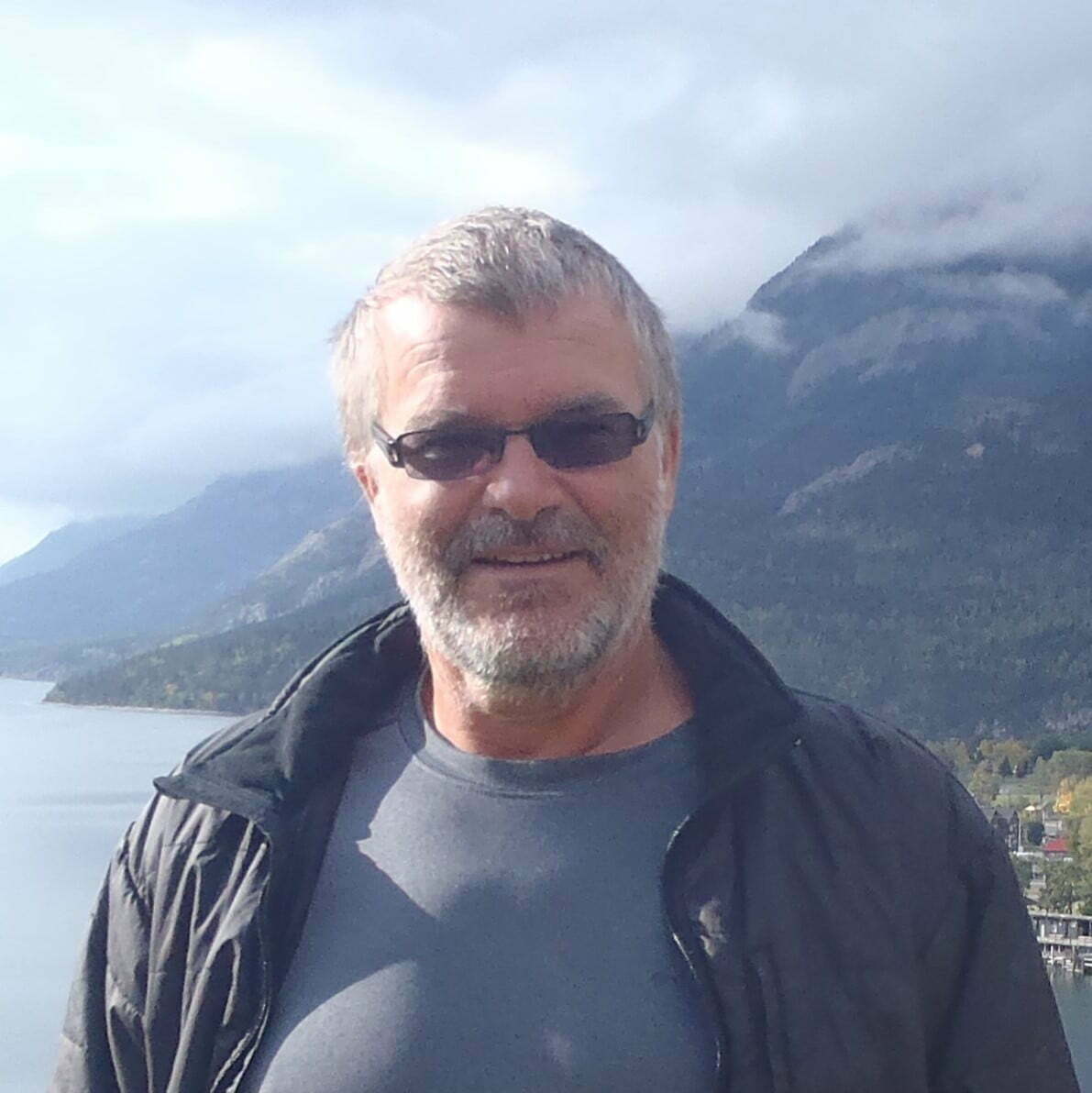 photo to man in front of sea side town in distance with mountains behind